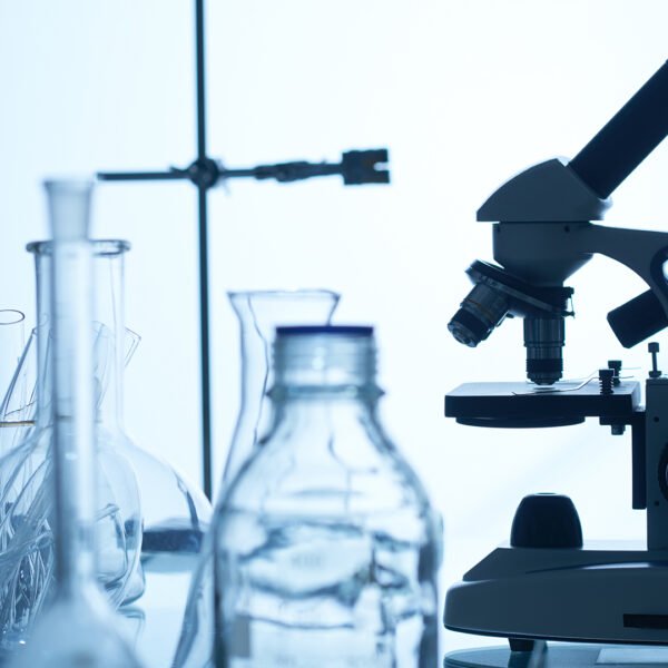 Laboratory bench with modern microscope, test tubes, glass bottles and flasks, white background